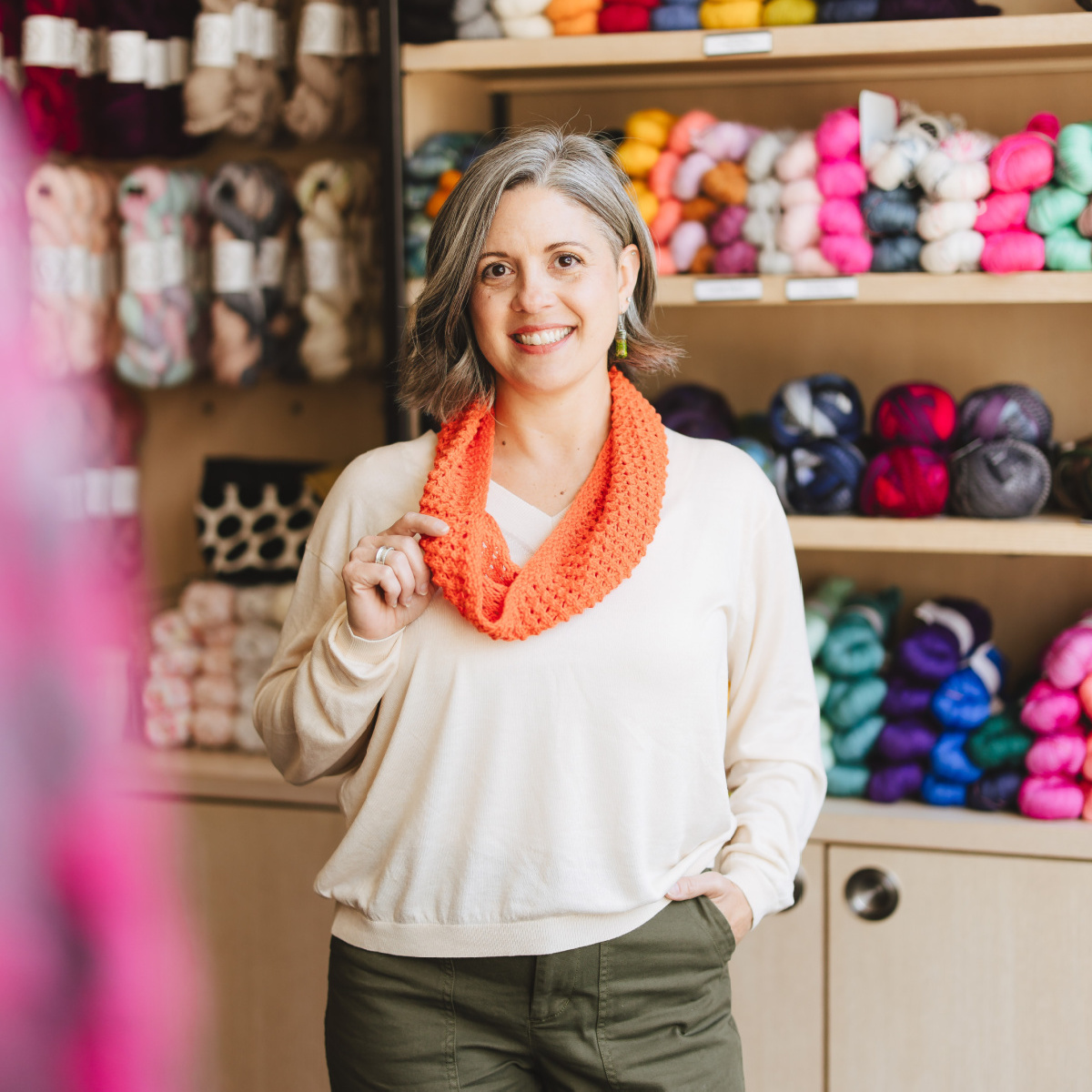 Crystal in coral cowl in front of yarn.