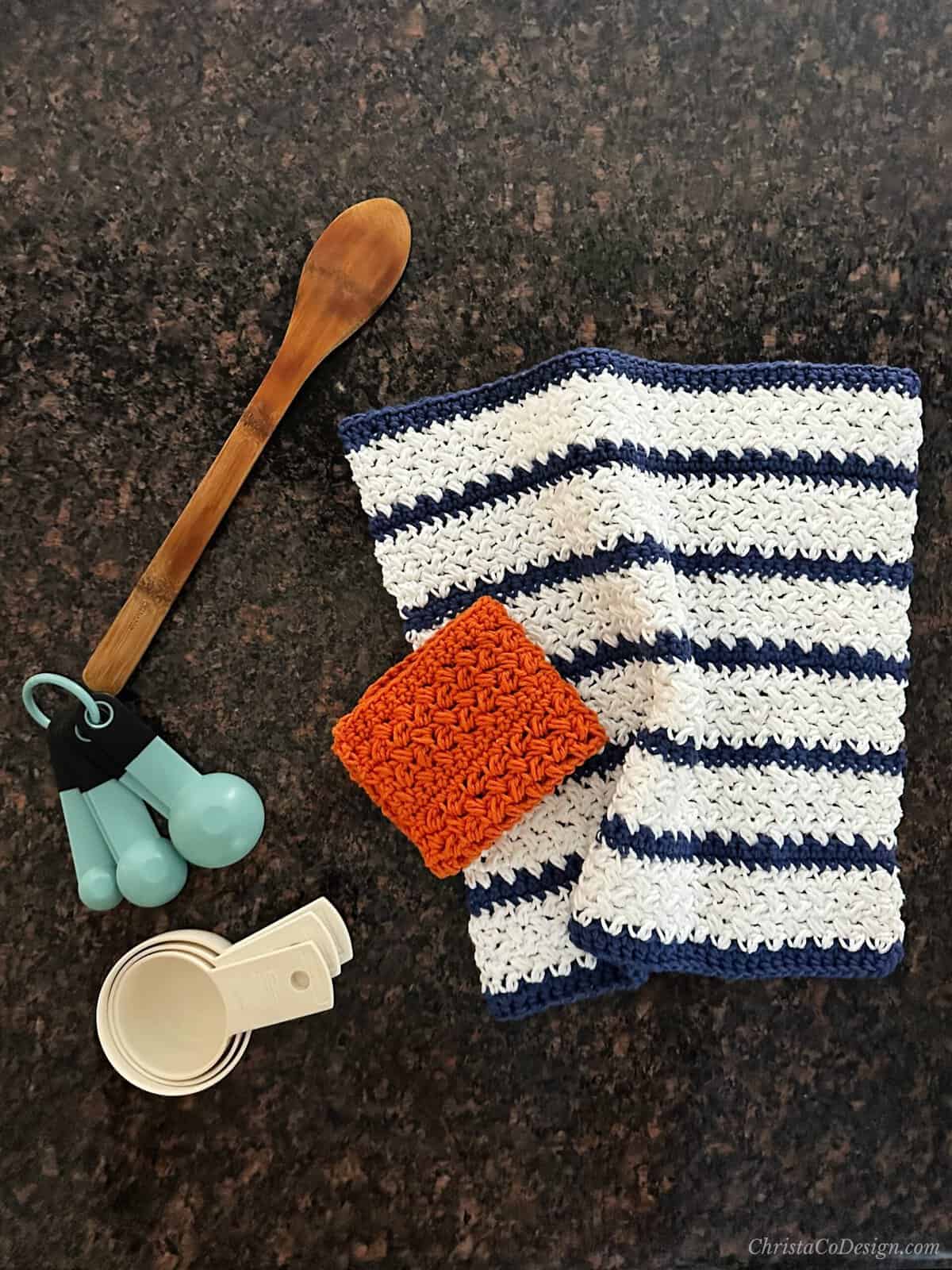 Crochet dish cloth in blue and white and an orange square with kitchen utensils.