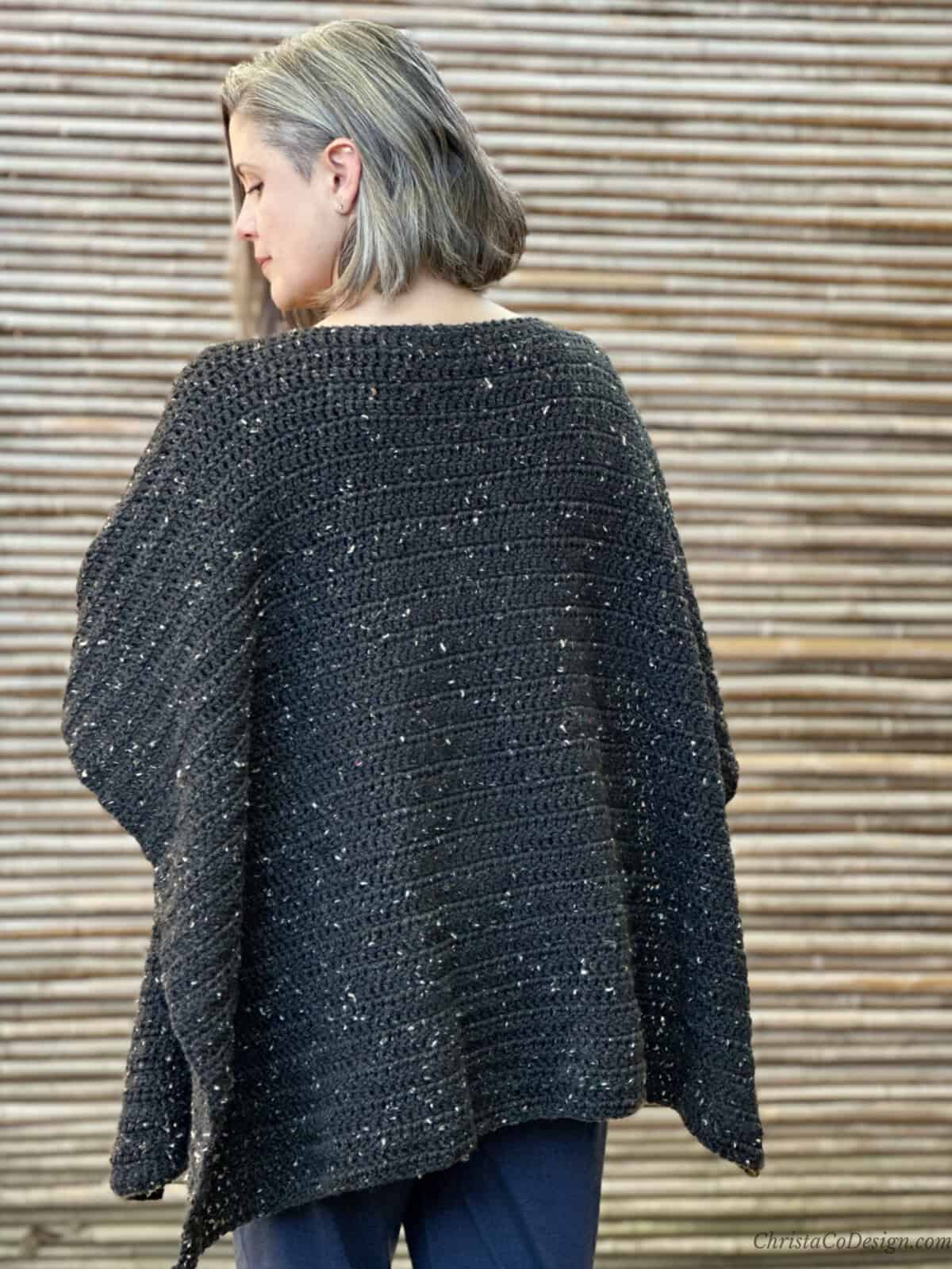 Woman in crochet poncho turned to show back.