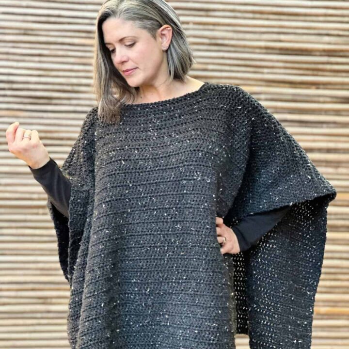 Woman looking down wearing black crochet poncho.