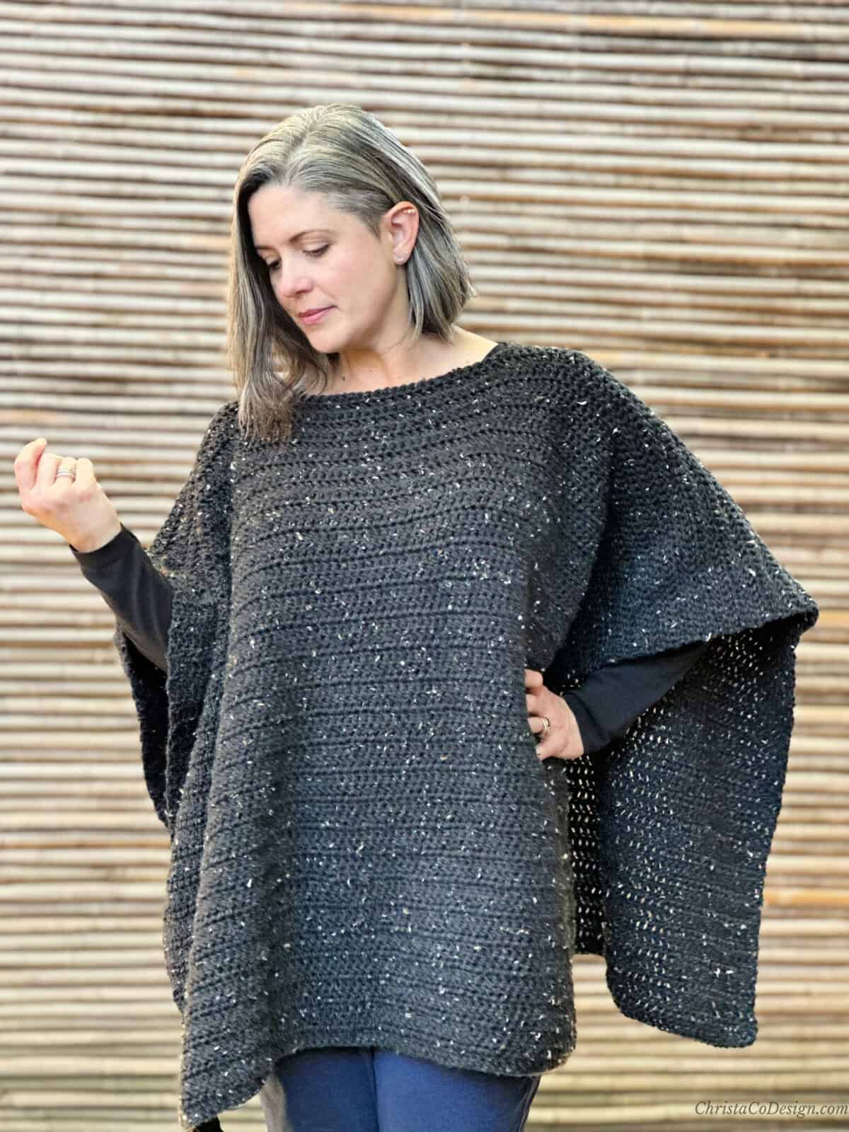 Woman looking down wearing black crochet poncho.