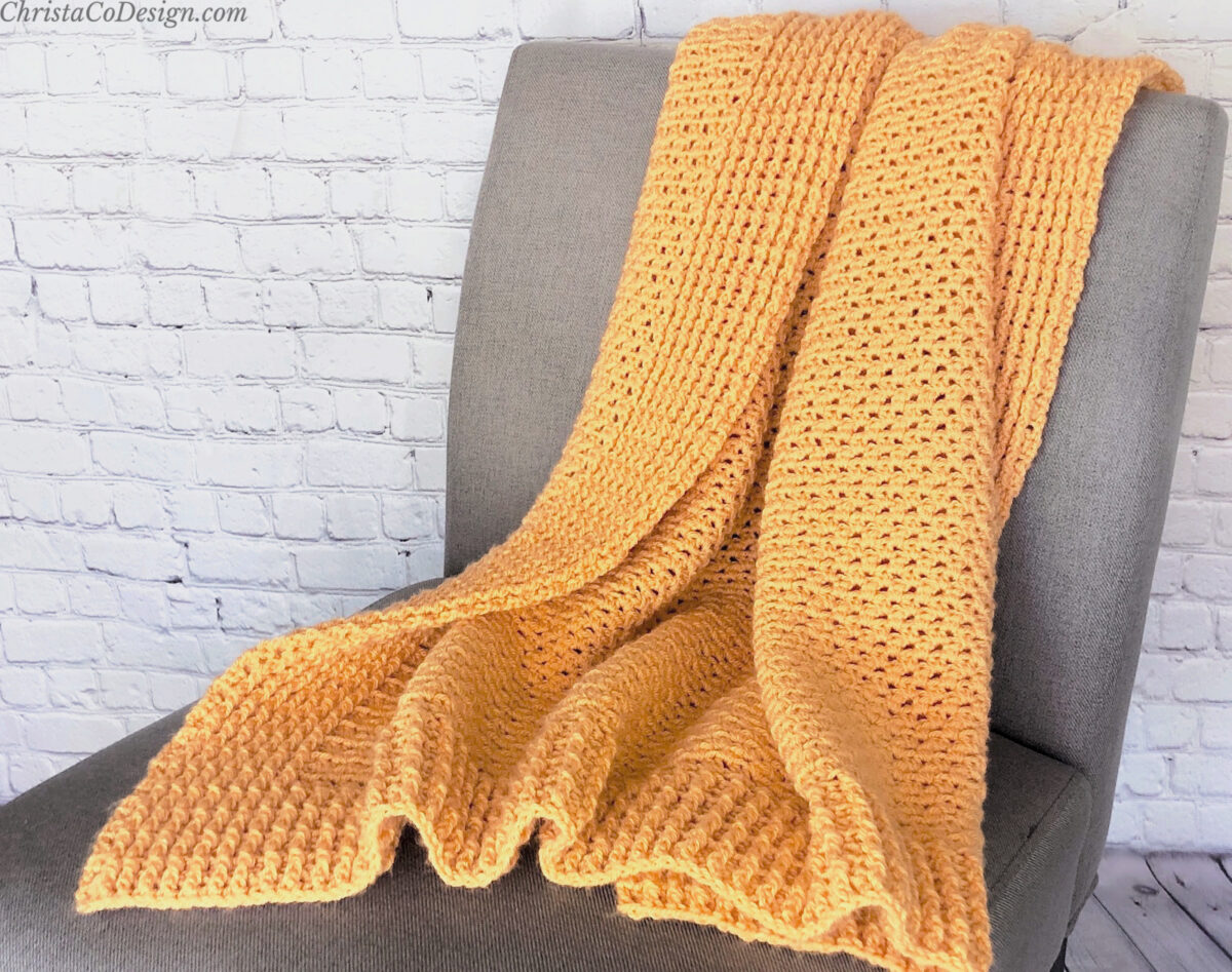 Orange crochet blanket draped on grey chair.