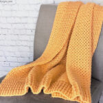 Orange crochet blanket draped on grey chair.
