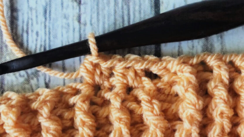 Crochet blanket in progress in orange yarn on crochet hook.
