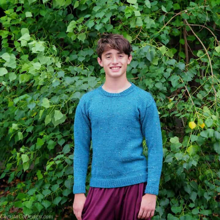Young man smiling in blue sweater.