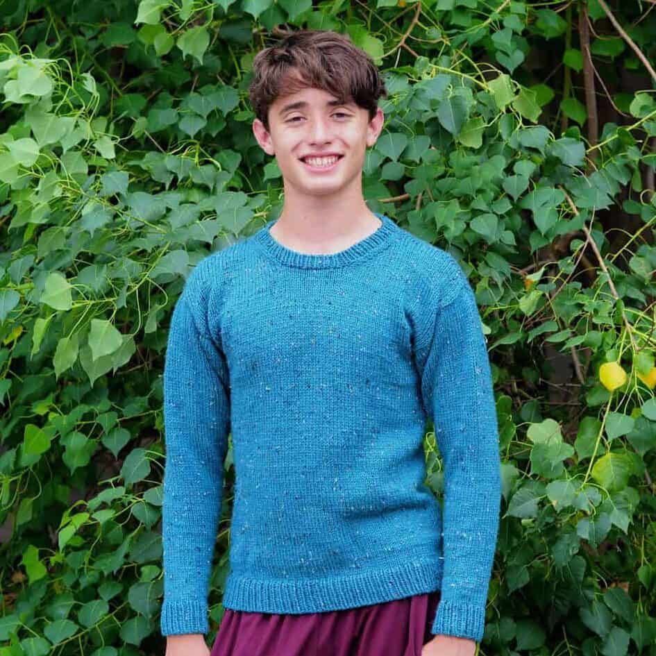 Young man smiling in blue sweater.