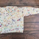 Colorful kids sweater laid out on wood table.