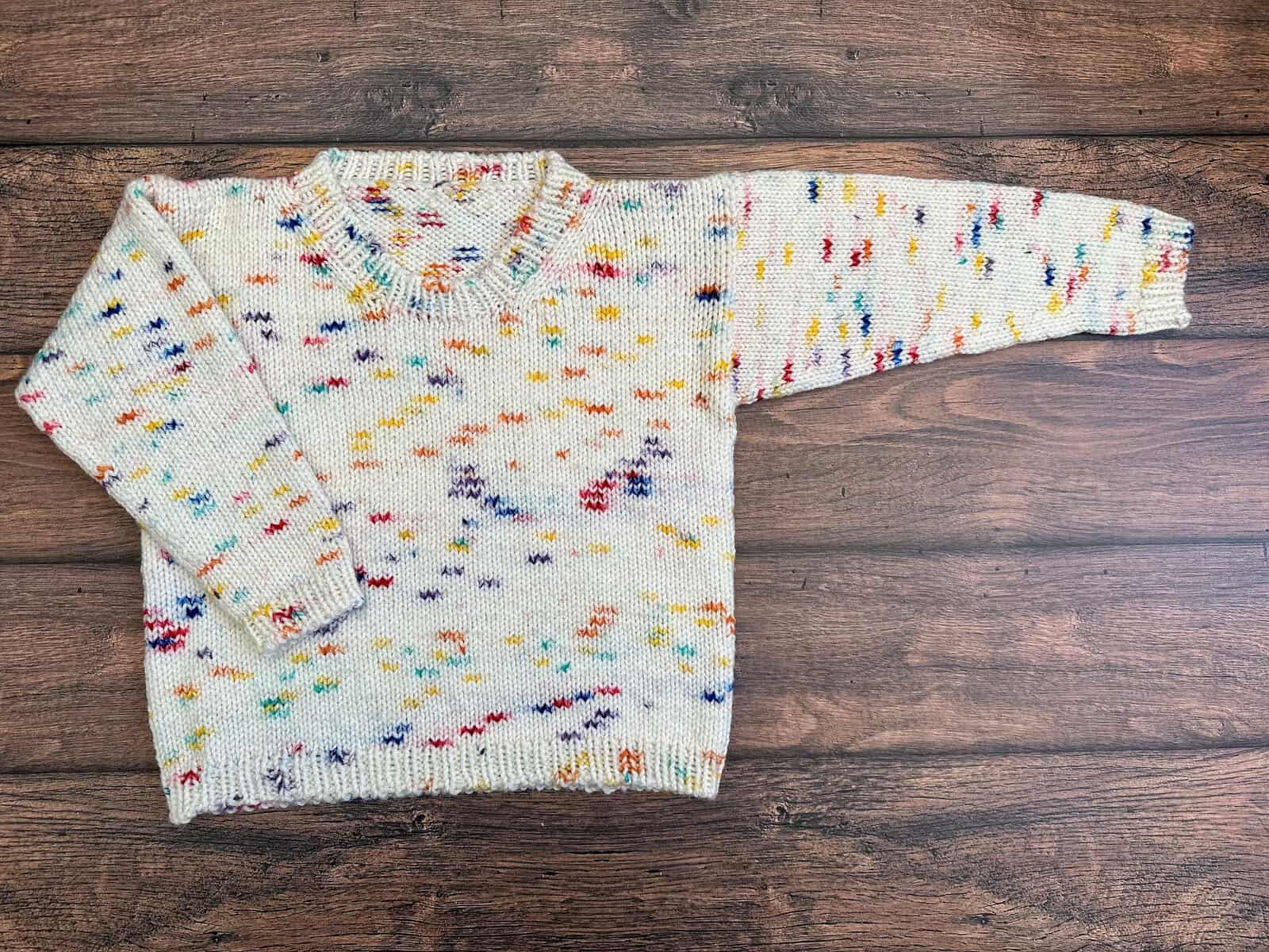 Colorful kids sweater laid out on wood table.