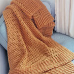 Crochet blanket in orange laid on blue chair.