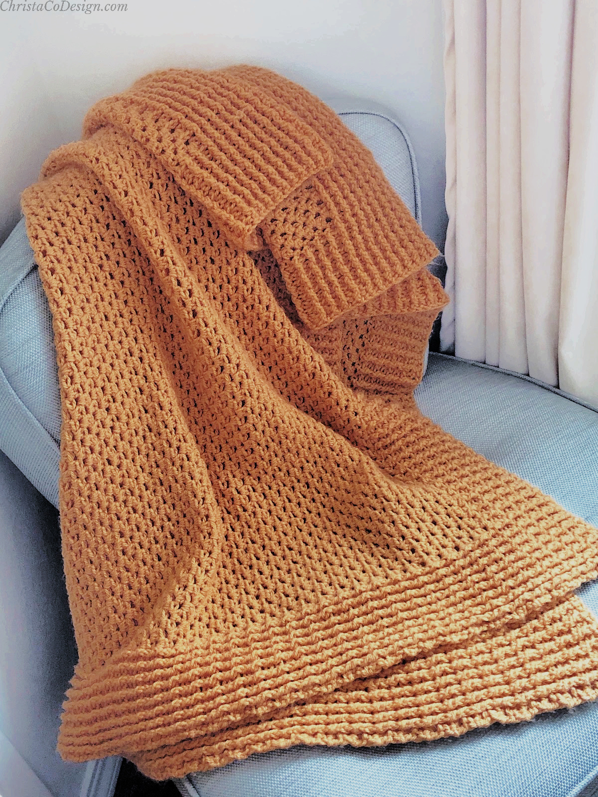 Crochet blanket in orange laid on blue chair.