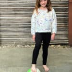 Girl in colorful knit sweater with foot on soccer ball.