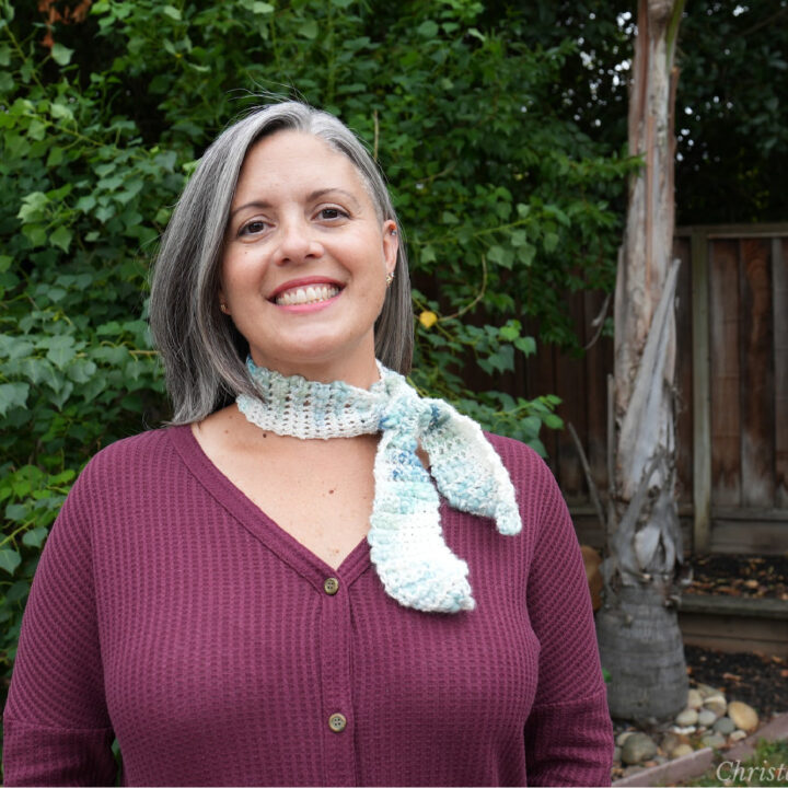 Woman smiling in crochet thin neck scarf outside.