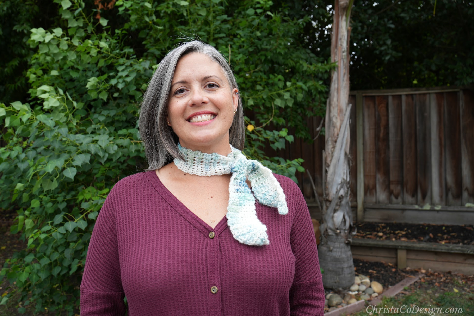 Woman smiling in crochet thin neck scarf outside.