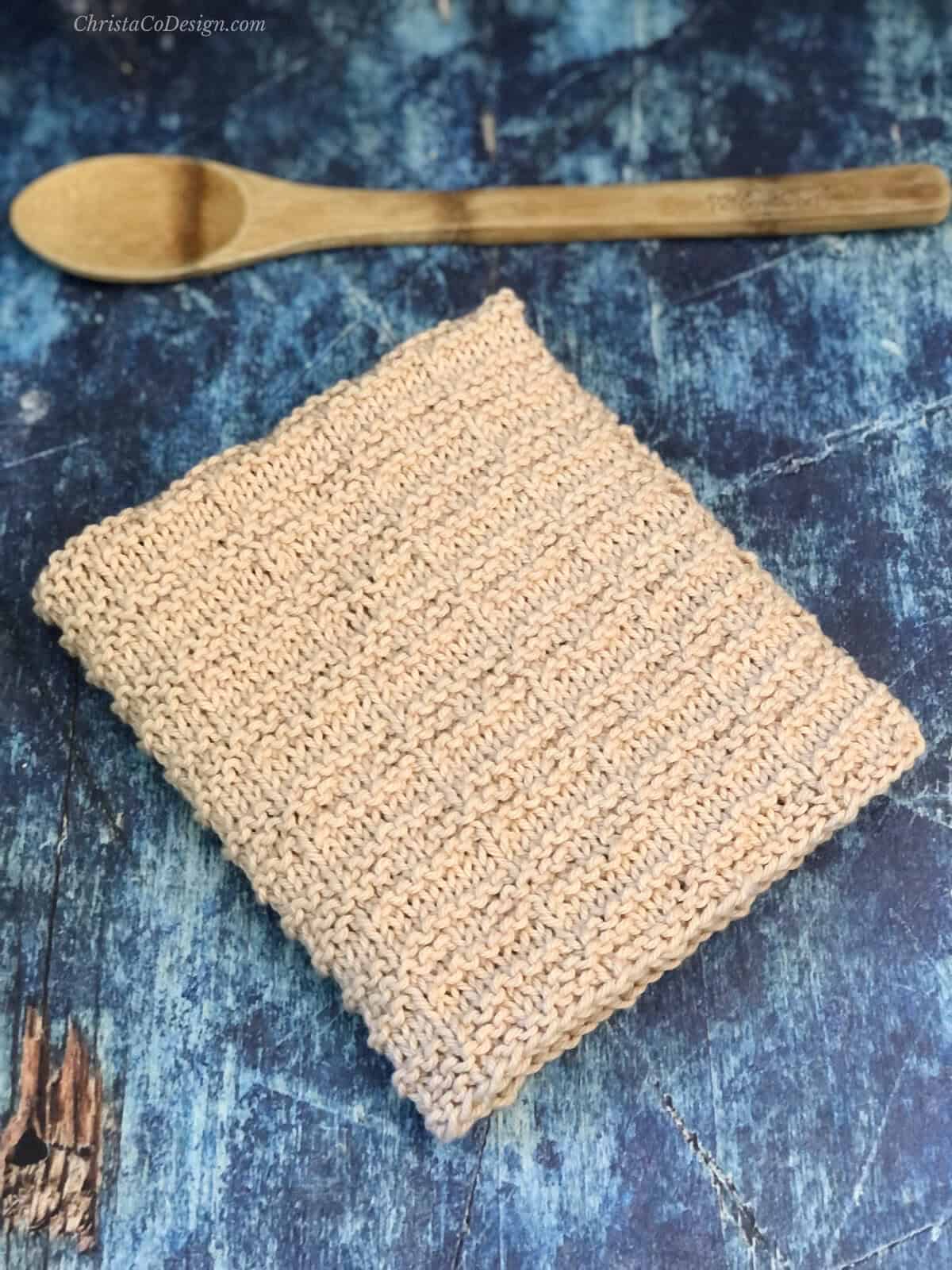 Folded dish towel next to kitchen spoon.