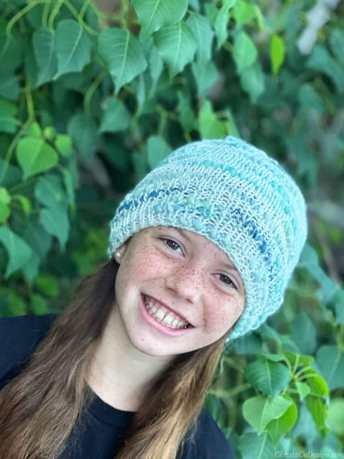 Angled photo of girl smiling in knit hat outside.