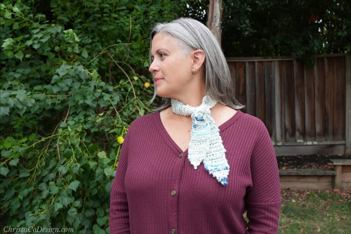 Woman turned to side with blue white skinny neck scarf on.