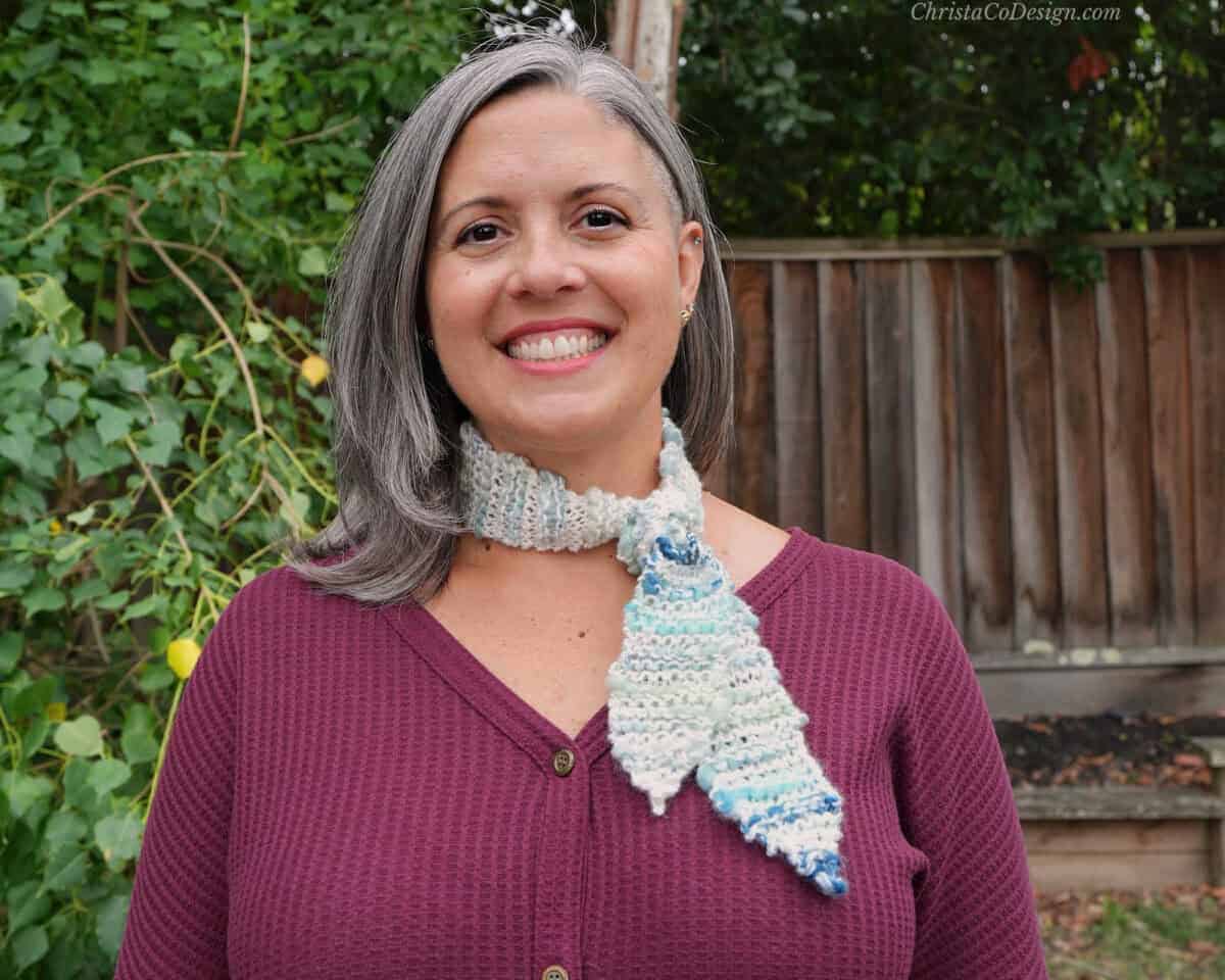 Woman smiling in red with knit scarf knotted at neck.